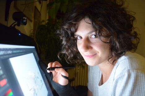 Anne Isensee blickt in die Kamera. In der rechten Hand hält die Animationskünstlerin einen digitalen Stift und zeichnet auf einem Tablet.