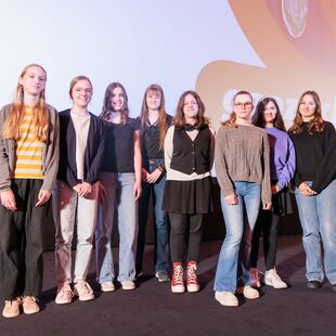 Acht Schülerinnen stehen auf der Bühne des Astor Kinos und blicken in die Kamera.