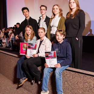 Die Jugendlichen des Filmteams sitzen und stehen auf der Bühne des Astor Kinos in Hannover und halten ihre Urkunden in die Kamera.