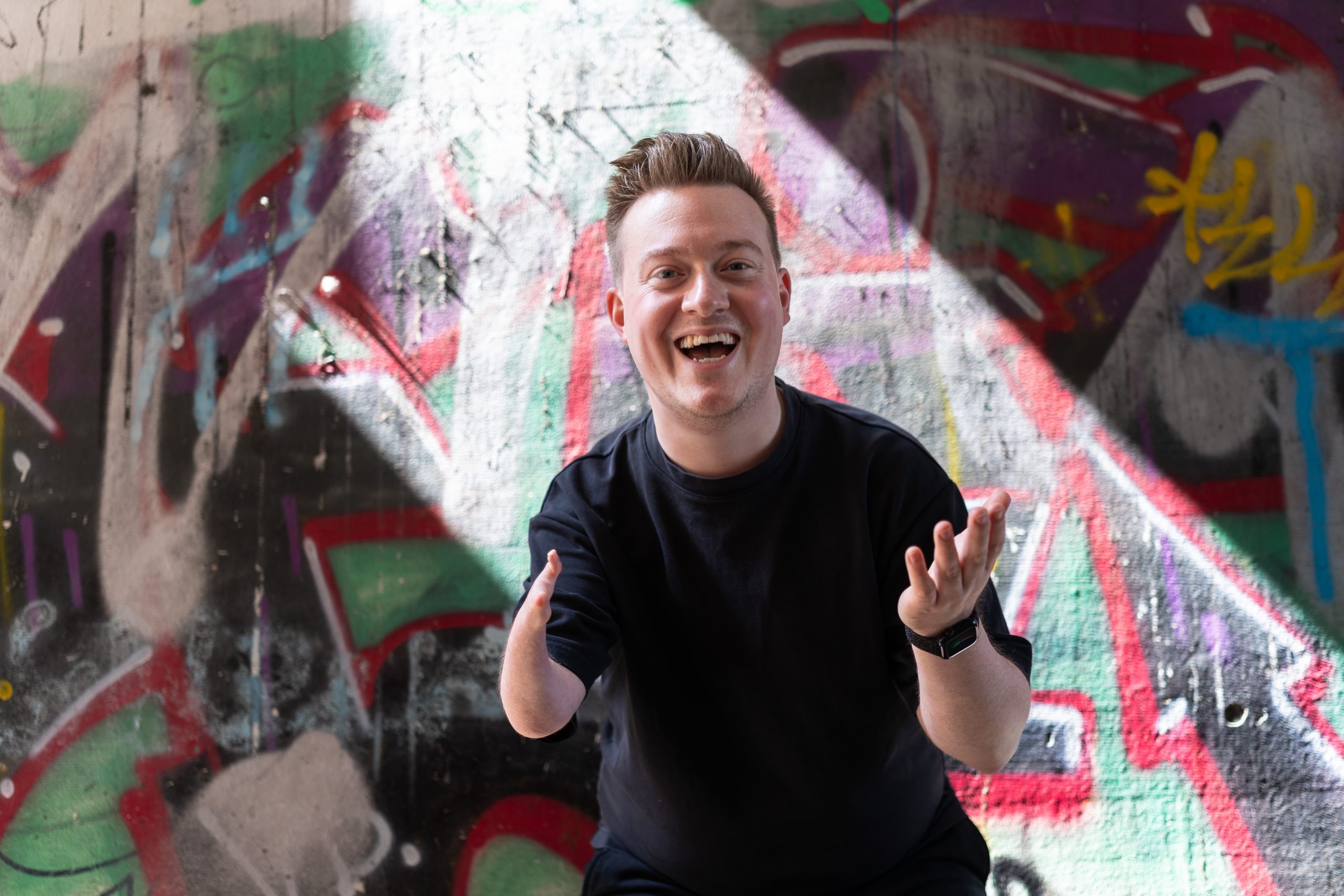 René Schaar, Botschafter von ganz schön unfair, lächelt in die Kamera. Im Hintergrund ist eine Wand mit Graffiti zu sehen.